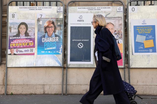 A pedestrian walks past campaign posters of mayoral canidates Sophia Chikirou (L) and Rachida Dati, displayed in central Paris on March 19, 2026, ahead of the second round of France's municipal elections. (Photo by Charlotte SIEMON / AFP)
