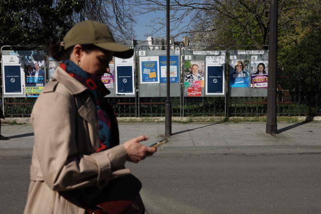 A pedestrian walks past campaign posters displayed in central Paris on March 19, 2026, ahead of the second round of France's municipal elections. (Photo by Charlotte SIEMON / AFP)