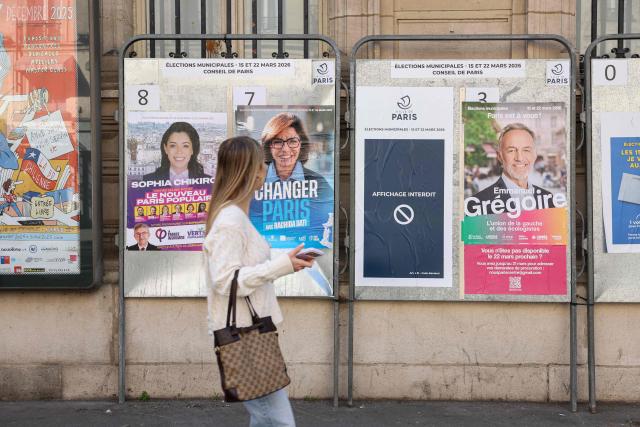 A pedestrian walks past campaign posters of mayoral canidates (From L) Sophia Chikirou, Rachida Dati and Emmanuel Gregoire, displayed in central Paris on March 19, 2026, ahead of the second round of France's municipal elections. (Photo by Charlotte SIEMON / AFP)