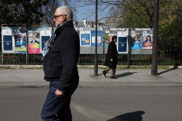 Pedestrians walk past campaign posters displayed in central Paris on March 19, 2026, ahead of the second round of France's municipal elections. (Photo by Charlotte SIEMON / AFP)