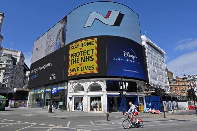 (FILES) A government sign advising people to "Stay Home, Protect the NHS, Save Lives" is displayed on the advertising boards in Piccadilly Circus in the spring sunshine on the bank holiday Monday in London on April 13, 2020. The UK's state-funded National Health Service (NHS) "came close to collapse" during the Covid-19 pandemic, a public inquiry concluded on March 19, 2026. A government slogan urging people to stay at home to "save lives" also "sent the message that healthcare was closed", according to the inquiry report. (Photo by Glyn KIRK / AFP)