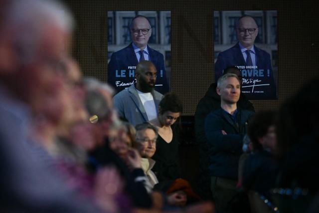 Supporters, standing in front of campaign posters depicting Le Havre's incumbent mayor and Horizons party candidate for his re-election Edouard Philippe, attend his campaign meeting in Le Havre, northeastern France on March 19, 2026, ahead of the second round of France's 2026 municipal elections. (Photo by LOU BENOIST / AFP)