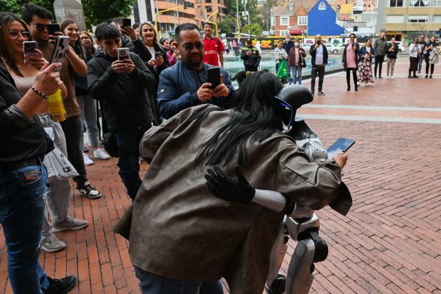 A humanoid robot called "Vicente" hugs a woman during a showcase on private security supported by artificial intelligence in Bogota on March 19, 2026. (Photo by Alejandro GONZALEZ / AFP)