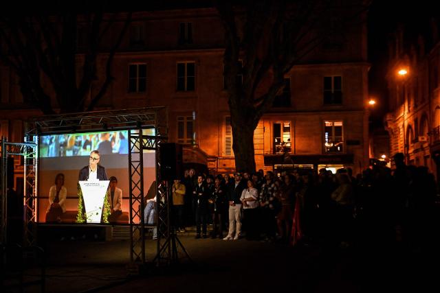 Supporters listen as they stand outside the venue of a campaign meeting of Bordeaux Mayor and candidate for his re-election Pierre Hurmic appearing on a giant screen during a campaign meeting in Bordeaux, southwestern France on March 19, 2026, ahead of the second round of France's 2026 municipal elections. (Photo by Christophe ARCHAMBAULT / AFP)