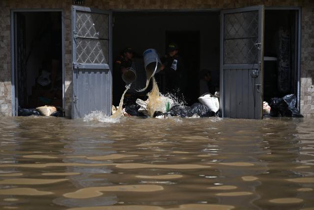 Police officers remove water from a house using buckets after heavy rains caused rivers to overflow in the Girardot neighborhood of Facatativa municipality, Cundinamarca department, Colombia, on March 19, 2026. (Photo by Raul ARBOLEDA / AFP)