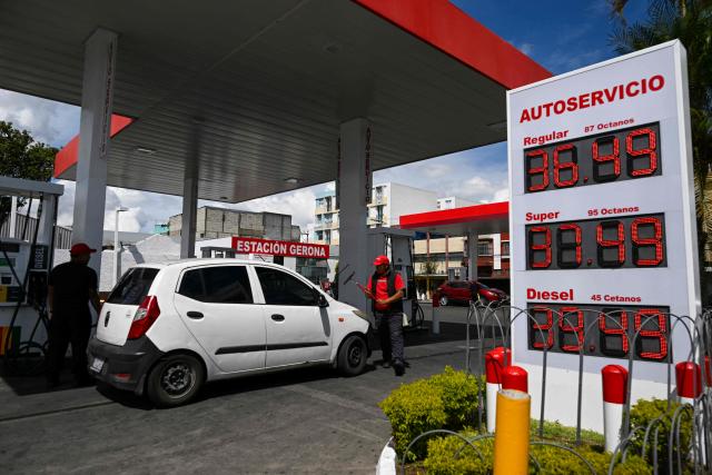 An attendant cleans a car as the new fuel prices are seen on a board at a gas station in Guatemala City on March 19, 2026. The prices of petroleum derivatives soared in Guatemala due to the war in the Middle East. (Photo by JOHAN ORDONEZ / AFP)