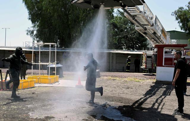 Soldiers wearing gasoline-resistant protective gear respond to an accident involving a gas tanker as part of ‘Exercise Ollamani’ at the Santa Lucia Military Base in the municipality of Zumpango, State of Mexico, Mexico, on March 19, 2026. "Exercise Ollamani" is organized by various institutions—including the Mexican Army, the National Guard, and the Attorney General's Office—and serves as an anti-terrorism drill designed to safeguard the 2026 World Cup. (Photo by Alfredo ESTRELLA / AFP)