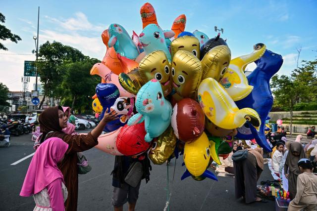 A Muslim women with her child buys a ballon after offering Eid al-Fitr morning prayer along a road in Surabaya on March 20, 2026, marking the end of holy month of Ramadan. (Photo by JUNI KRISWANTO / AFP)