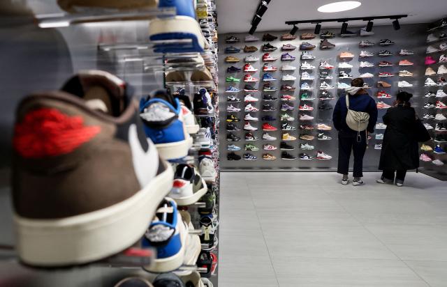 Clients look at sneakers displayed at the Swave store of founder Hugo Carvalho, in Paris March 12, 2026. Teleshopping isn’t dead; it’s just moved to mobile: combining live video with instant purchasing, ‘live shopping’ is revolutionising online retail, prompting tech giants, brands and small shops alike to get on board. ‘Starting price: one euro... 20 seconds to bid. 3, 2, 1, go!’ Sitting in front of his multiple screens, Hugo Carvalho, founder of the Parisian shop Swave, which specialises in collectable trainers, is shouting himself hoarse live on the Whatnot app. (Photo by ALAIN JOCARD / AFP)