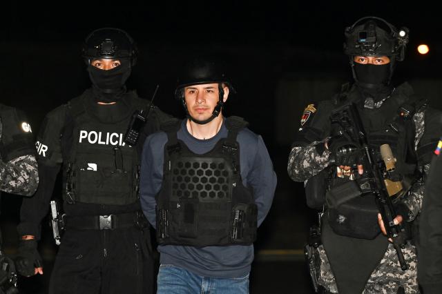 Ecuador’s police officers escort Ecuadorian drug trafficker Angel Aguilar, alias ‘Lobo Menor’, as he arrives at the Aeropolicial facilities at the airport in Guayaquil on March 19, 2026. Colombia’s migration authority reported on Marche 18, 2026 the arrest of Ecuadorian drug trafficker Angel Aguilar, who is linked to the assassination in Quito of presidential candidate Fernando Villavicencio one week before the 2023 elections. (Photo by Marcos PIN / AFP)