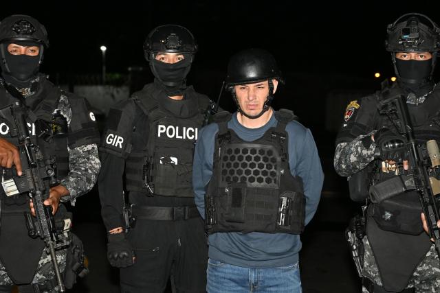 Ecuador’s police officers escort Ecuadorian drug trafficker Angel Aguilar, alias ‘Lobo Menor’, as he arrives at the Aeropolicial facilities at the airport in Guayaquil on March 19, 2026. Colombia’s migration authority reported on Marche 18, 2026 the arrest of Ecuadorian drug trafficker Angel Aguilar, who is linked to the assassination in Quito of presidential candidate Fernando Villavicencio one week before the 2023 elections. (Photo by Marcos PIN / AFP)