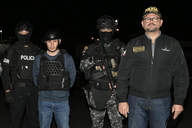 TOPSHOT - Ecuador’s police officers, alongside Interior Minister John Reimberg (R), pose with Ecuadorian drug trafficker Angel Aguilar (C), alias ‘Lobo Menor’, as he arrives at the Aeropolicial facilities at the airport in Guayaquil on March 19, 2026. Colombian immigration authorities said on March 18, 2026, they had arrested an Ecuadoran drug trafficker linked to the 2023 murder of a popular candidate just before Ecuador's presidential election. (Photo by Marcos PIN / AFP)