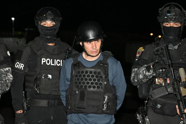 TOPSHOT - Ecuador’s police officers escort Ecuadorian drug trafficker Angel Aguilar, alias ‘Lobo Menor’, as he arrives at the Aeropolicial facilities at the airport in Guayaquil on March 19, 2026. Colombia’s migration authority reported on Marche 18, 2026 the arrest of Ecuadorian drug trafficker Angel Aguilar, who is linked to the assassination in Quito of presidential candidate Fernando Villavicencio one week before the 2023 elections. (Photo by Marcos PIN / AFP)