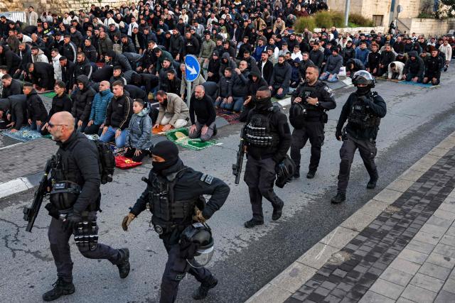 TOPSHOT - Israeli security forces walk past Muslim worshippers gathering outside the Jerusalem old city walls on March 20, 2026 to attend attend the early morning prayers for Eid al-Fitr, marking the end of the holy month of Ramadan. Holy sites such as the Aqsa mosque compound in Jerusalem's old city have remained closed for security reasons since the outbreak of the Middle East war on February 28, when Israel and the US launched strikes on Iran. (Photo by AHMAD GHARABLI / AFP)