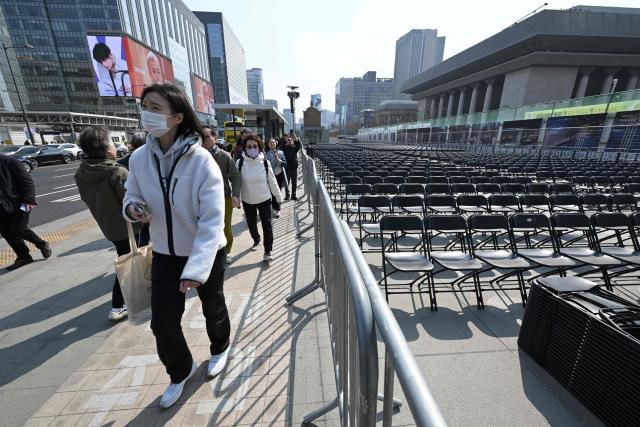 People walk past rows of chairs set up for the comeback concert of K-pop boy group BTS at Gwanghwamun Square in Seoul on March 20, 2026. K-pop megastars BTS released a new album on March 20, billed as reflecting the maturing boy band's Korean roots and identity, as buzz built ahead of their open-air comeback concert in the heart of Seoul. (Photo by Jung Yeon-je / AFP)