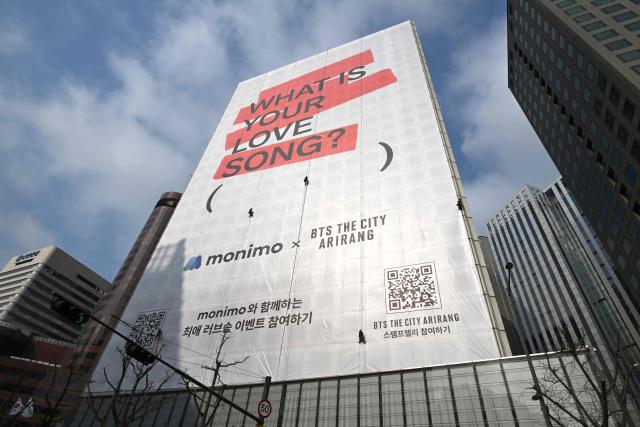 Workers install a large banner promoting the new album of K-pop boy group BTS on the exterior wall of a building in Seoul on March 20, 2026. K-pop megastars BTS released a new album on March 20, billed as reflecting the maturing boy band's Korean roots and identity, as buzz built ahead of their open-air comeback concert in the heart of Seoul. (Photo by Jung Yeon-je / AFP)