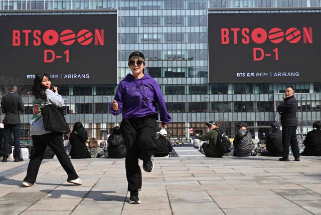 A BTS fan dances in front of electronic screens promoting the comeback concert of K-pop boy group BTS at Gwanghwamun Square in Seoul on March 20, 2026. K-pop megastars BTS released a new album on March 20, billed as reflecting the maturing boy band's Korean roots and identity, as buzz built ahead of their open-air comeback concert in the heart of Seoul. (Photo by Jung Yeon-je / AFP)