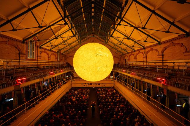 Members of Kantos Chamber Choir perform choral works inspired by the Sun, beneath the artwork entitled 'Helios' by artist Luke Jerram in Victoria Baths, Manchester, north west England on March 19, 2026. The artwork 'Helios' measures seven metres in diameter and has been constructed using approximately 400,000 detailed photographs of the Sun's surface. The piece is a representation of the Sun at an approximate scale of 1:200 million, where each centimetre on the artwork represents 2000km on the Sun's surface. (Photo by Oli SCARFF / AFP)