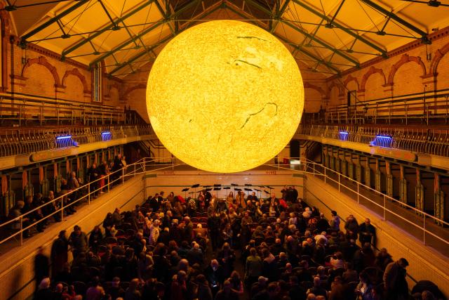 Audience members depart following Kantos Chamber Choir's performance of choral works inspired by the Sun, beneath the artwork entitled 'Helios' by artist Luke Jerram, in Victoria Baths, Manchester, north west England on March 19, 2026. The artwork 'Helios' measures seven metres in diameter and has been constructed using approximately 400,000 detailed photographs of the Sun's surface. The piece is a representation of the Sun at an approximate scale of 1:200 million, where each centimetre on the artwork represents 2000km on the Sun's surface. (Photo by Oli SCARFF / AFP)