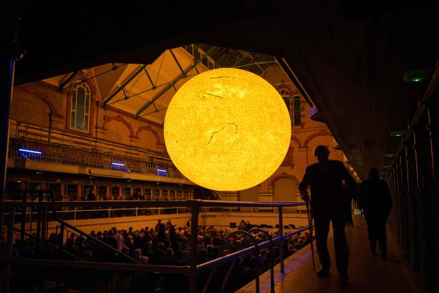 Audience members prepare to take their seats before Kantos Chamber Choir's performance of choral works inspired by the Sun, beneath the artwork entitled 'Helios' by artist Luke Jerram, in Victoria Baths, Manchester, north west England on March 19, 2026. The artwork 'Helios' measures seven metres in diameter and has been constructed using approximately 400,000 detailed photographs of the Sun's surface. The piece is a representation of the Sun at an approximate scale of 1:200 million, where each centimetre on the artwork represents 2000km on the Sun's surface. (Photo by Oli SCARFF / AFP)