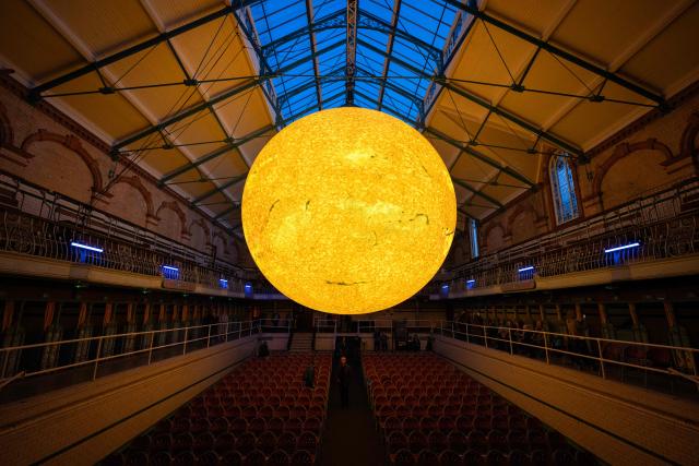 Audience members prepare to take their seats before Kantos Chamber Choir's performance of choral works inspired by the Sun, beneath the artwork entitled 'Helios' by artist Luke Jerram, in Victoria Baths, Manchester, north west England on March 19, 2026. The artwork 'Helios' measures seven metres in diameter and has been constructed using approximately 400,000 detailed photographs of the Sun's surface. The piece is a representation of the Sun at an approximate scale of 1:200 million, where each centimetre on the artwork represents 2000km on the Sun's surface. (Photo by Oli SCARFF / AFP)