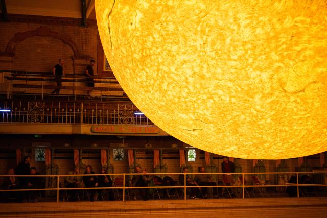Audience members take their seats before Kantos Chamber Choir's performance of choral works inspired by the Sun, beneath the artwork entitled 'Helios' by artist Luke Jerram, in Victoria Baths, Manchester, north west England on March 19, 2026. The artwork 'Helios' measures seven metres in diameter and has been constructed using approximately 400,000 detailed photographs of the Sun's surface. The piece is a representation of the Sun at an approximate scale of 1:200 million, where each centimetre on the artwork represents 2000km on the Sun's surface. (Photo by Oli SCARFF / AFP)