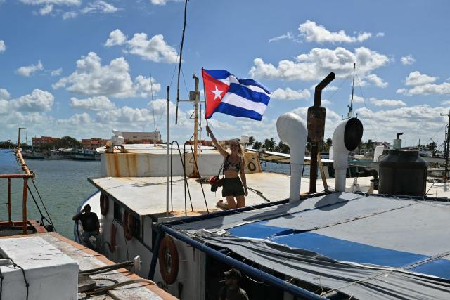 An activist of NuestraAmerica Iniciative flutters a Cuban flag on a boat nicknamed "Grandma 2" that starts its journey to take 30 tons of humanitarian aid to Cuba, as part of the Convoy to Cuba, organised by left-wing activists from various countries in the Americas and Europe, in Puerto Progreso, Yucatan state, Mexico, on March 20, 2026. The first shipment of international aid for crisis-hit Cuba arrived in the country from Europe on March 18, 2026 in the shape of five tons of medical supplies. (Photo by YURI CORTEZ / AFP)