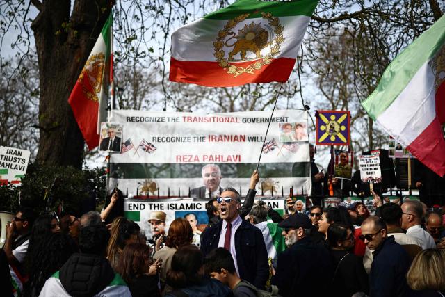 Anti-Iranian regime protesters wave Iranian flags before the 1979 revolution with the Lion and Sun emblem at a protest, outside the Iranian Embassy in central London on March 20, 2026. (Photo by Henry NICHOLLS / AFP)