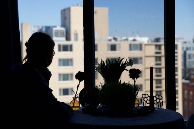 An Iranian journalist in exile (name withheld due to security reasons) sits at a Haft Sin table at their residence awaiting the Persian New Year, Nowruz, on March 20, 2026, in Washington, DC. Iranian families in the Washington, DC, area are trying to maintain cultural traditions while following the news of the ongoing conflict in Iran. From specialty Persian markets to community gatherings, preparations continue with a mix of resilience and concern, as the diaspora balances celebration with anxiety for loved ones in a country facing escalating violence. (Photo by Amid FARAHI / AFP)