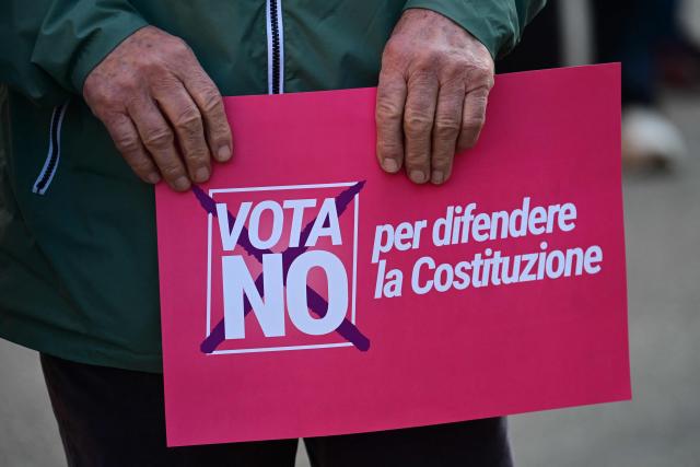 A person holds a placard reading "Vote NO to defend the Constitution" before a campaign meeting of Italian Democratic Party (PD) ahead of the Italian referendum on Justice reform, in Milan on March 20, 2026. Italian citizens will vote on 22 and 23 March 2026, in a confirmatory referendum regarding a constitutional reform of the judicial system proposed by the government. The reform centers on the "separation of careers" between judges and public prosecutors. (Photo by Stefano Rellandini / AFP)