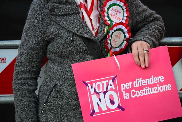 A person holds a placard reading "Vote NO to defend the Constitution" before a campaign meeting of Italian Democratic Party (PD) ahead of the Italian referendum on Justice reform, in Milan on March 20, 2026. Italian citizens will vote on 22 and 23 March 2026, in a confirmatory referendum regarding a constitutional reform of the judicial system proposed by the government. The reform centers on the "separation of careers" between judges and public prosecutors. (Photo by Stefano Rellandini / AFP)