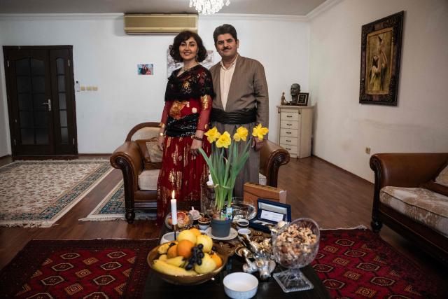 Former Kurdish fighter Saad Qazi (R) and his wife Parang Jahani pose with their traditional costumes at their apartment during the Nowruz celebrations in Erbil, the capital of Iraq's autonomous Kurdish region, on March 19, 2026. In Iraq's northern Kurdistan region, women perform a traditional dance, their long dresses spinning, gold tassels and heavy necklaces catching the firelight, as smaller crowds than usual celebrate Nowruz, overshadowed by the Middle East conflict. (Photo by Ozan KOSE / AFP)