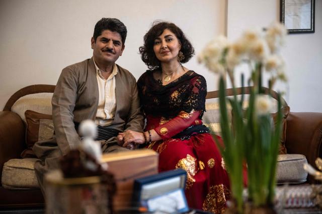 Former Kurdish fighter Saad Qazi (L) and his wife Parang Jahani pose with their traditional costumes at their apartment during the Nowruz celebrations in Erbil, the capital of Iraq's autonomous Kurdish region, on March 19, 2026. In Iraq's northern Kurdistan region, women perform a traditional dance, their long dresses spinning, gold tassels and heavy necklaces catching the firelight, as smaller crowds than usual celebrate Nowruz, overshadowed by the Middle East conflict. (Photo by Ozan KOSE / AFP)