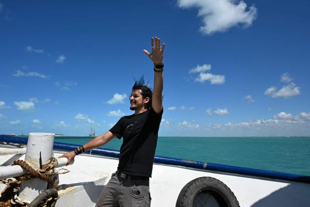 An activist gestures onboard the Mexican boat nicknamed "Grandma 2" taking 30 tons of humanitarian aid to Cuba, as part of the Convoy to Cuba, organised by left-wing activists from various countries in the Americas and Europe, off Puerto Progreso, Yucatan state, Mexico, on March 20, 2026. The first shipment of international aid for crisis-hit Cuba arrived in the country from Europe on March 18, 2026 in the shape of five tons of medical supplies. (Photo by YURI CORTEZ / AFP)