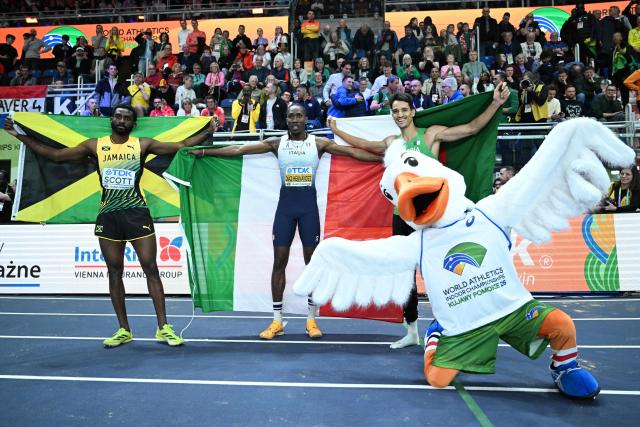 Jamaica's Jordan Scott (L), Italy's Andy Diaz Hernandez and Algeria's Yasser Mohammed Triki celebrate with country flags after competing in the men's final triple jump event during the World Athletics Indoor Championships Kujawy Pomorze 2026 in Torun, Poland on March 20, 2026. (Photo by Kirill KUDRYAVTSEV / AFP)