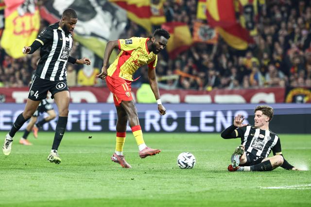 Lens' French forward #11 Odsonne Edouard (C) kicks the ball and scores his team's fourth goal next to Angers' French-Guinean defender #29 Ousmane Camara (L) and Angers' French defender #20 Marius Louer (R) during the French L1 football match between RC Lens and SCO Angers at the Stade Bollaert-Delelis in Lens, northern France, on March 20, 2026. (Photo by Sameer Al-DOUMY / AFP)