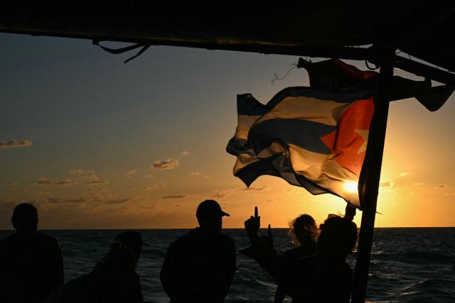 Silhouettes of activists and a Cuban flag are seen aboard the Mexican boat nicknamed ‘Grandma 2’, already in the Caribbean Sea after setting sail with 30 tons of humanitarian aid bound for Cuba, as part of the Convoy to Cuba organized by left-wing activists from several countries in the Americas and Europe, in Caribbean Sea on March 20, 2026. The first shipment of international aid for crisis-hit Cuba arrived in the country from Europe on March 18, 2026 in the shape of five tons of medical supplies. (Photo by YURI CORTEZ / AFP)