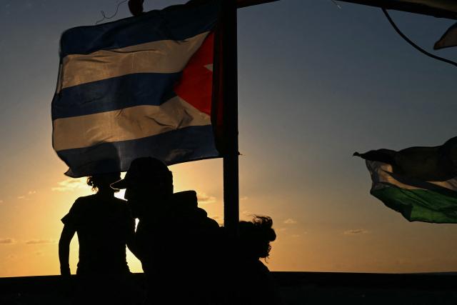 Silhouettes of activists and a Cuban flag are seen aboard the Mexican boat nicknamed ‘Grandma 2’, already in the Caribbean Sea after setting sail with 30 tons of humanitarian aid bound for Cuba, as part of the Convoy to Cuba organized by left-wing activists from several countries in the Americas and Europe, in Caribbean Sea on March 20, 2026. The first shipment of international aid for crisis-hit Cuba arrived in the country from Europe on March 18, 2026 in the shape of five tons of medical supplies. (Photo by YURI CORTEZ / AFP)