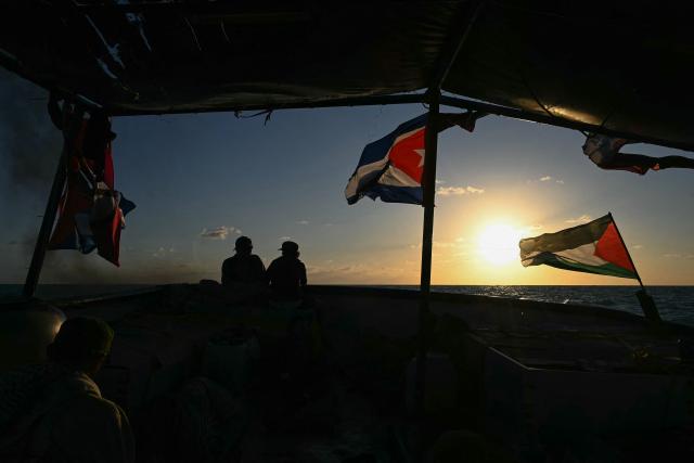 Silhouettes of activists and a Cuban flag are seen aboard the Mexican boat nicknamed ‘Grandma 2’, already in the Caribbean Sea after setting sail with 30 tons of humanitarian aid bound for Cuba, as part of the Convoy to Cuba organized by left-wing activists from several countries in the Americas and Europe, in Caribbean Sea on March 20, 2026. The first shipment of international aid for crisis-hit Cuba arrived in the country from Europe on March 18, 2026 in the shape of five tons of medical supplies. (Photo by YURI CORTEZ / AFP)