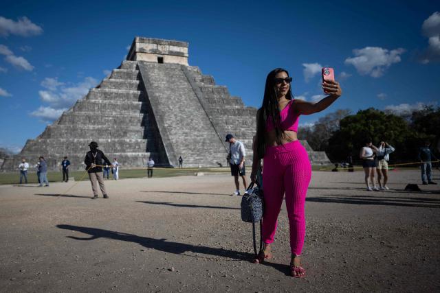 A woman poses for a photo a people gather to watch as the shape of a serpent is cast via shadows on the El Castillo pyramid in Chichen Itza on the day of the equinox, Yucatan State, Mexico, on March 20, 2026. The Chichen Itza equinox is a twice-yearly event (spring and fall) where sunlight and shadow create the illusion of a serpent, the deity Kukulcan on the world famous landmark, Chichen Itza’s main pyramid. (Photo by Carl de Souza / AFP)
