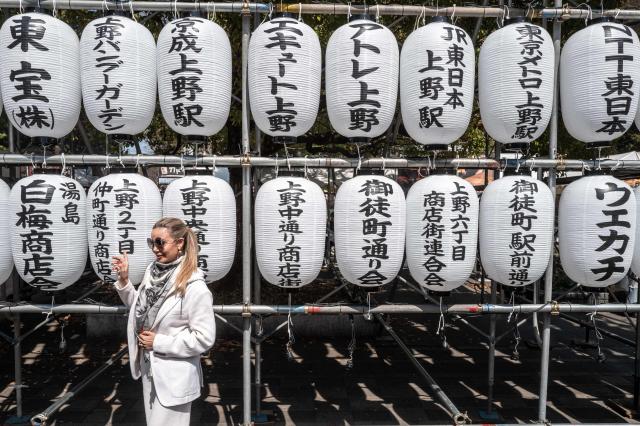 A woman poses for pictures with lanterns at Ueno park in Tokyo on March 21, 2026. (Photo by Philip FONG / AFP)