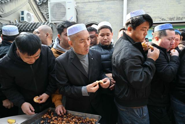 Muslim devotees eat food during Eid Al-Fitr celebrations, which marks the end of the Islamic holy fasting month of Ramadan, at a mosque in Beijing on March 21, 2026. (Photo by ADEK BERRY / AFP)
