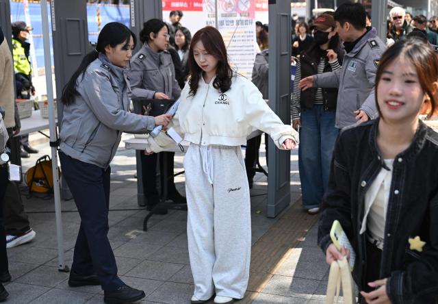 BTS fans pass through a security check as police officers inspect visitors at the venue of the comeback concert of K-pop boy group BTS in downtown Seoul on March 21, 2026. The world's biggest boy band BTS reunites on March 21, for an open-air comeback concert in the heart of Seoul, expected to draw around 250,000 people and beamed live across the globe. (Photo by Jung Yeon-je / AFP)