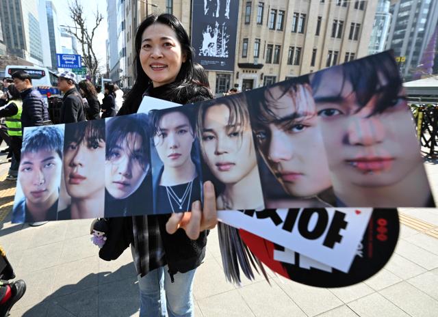 A woman holds a banner showing pictures of BTS members as BTS fans arrive at the venue of the comeback concert of K-pop boy group BTS in downtown Seoul on March 21, 2026. The world's biggest boy band BTS reunites on March 21, for an open-air comeback concert in the heart of Seoul, expected to draw around 250,000 people and beamed live across the globe. (Photo by Jung Yeon-je / AFP)