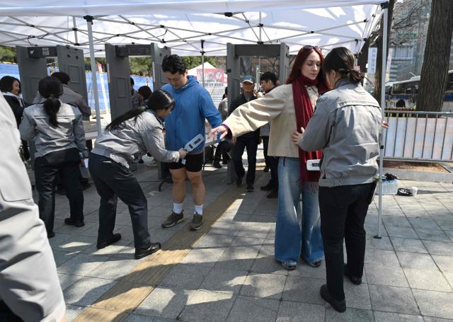 BTS fans pass through a security check as police officers inspect visitors at the venue of the comeback concert of K-pop boy group BTS in downtown Seoul on March 21, 2026. The world's biggest boy band BTS reunites on March 21, for an open-air comeback concert in the heart of Seoul, expected to draw around 250,000 people and beamed live across the globe. (Photo by Jung Yeon-je / AFP)