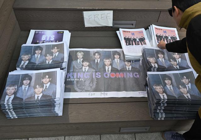 A woman picks up extra edition newspapers reporting the comeback of BTS near the venue of the comeback concert of K-pop boy group BTS in downtown Seoul on March 21, 2026. The world's biggest boy band BTS reunites on March 21, for an open-air comeback concert in the heart of Seoul, expected to draw around 250,000 people and beamed live across the globe. (Photo by Jung Yeon-je / AFP)