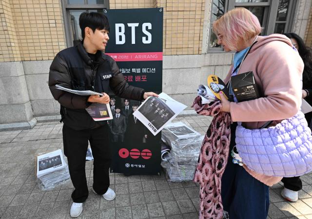 A man hands out extra edition newspapers reporting the comeback of BTS near the venue of the comeback concert of K-pop boy group BTS in downtown Seoul on March 21, 2026. The world's biggest boy band BTS reunites on March 21, for an open-air comeback concert in the heart of Seoul, expected to draw around 250,000 people and beamed live across the globe. (Photo by Jung Yeon-je / AFP)