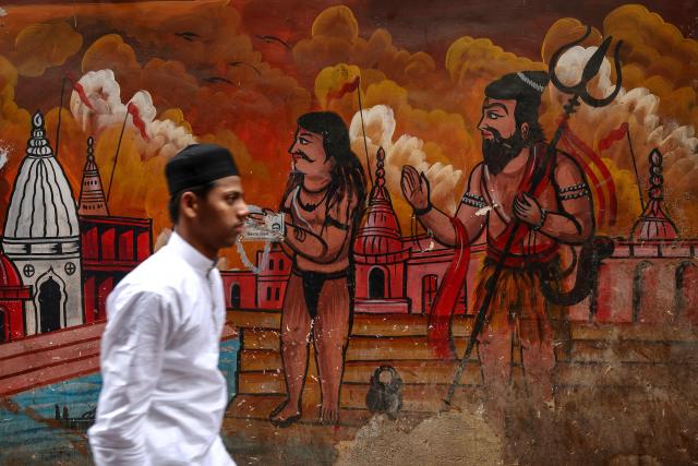 A Muslim devotee walks past a mural as he leaves after offering Eid al-Fitr prayers, which marks the end of the Islamic holy fasting month of Ramadan, at Alamgir Mosque along the banks of the river Ganges in Varanasi on March 21, 2026. (Photo by Niharika KULKARNI / AFP)