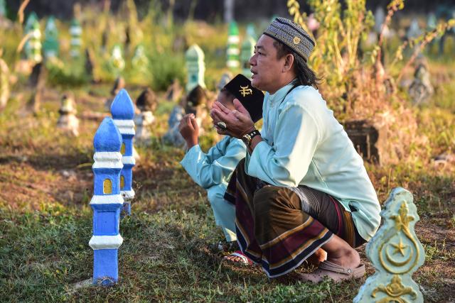 Thai Muslims pray before the grave of their relative during Eid al-Fitr, which marks the end of the holy fasting month of Ramadan, at Ban Yakang Cemetery in the southern Thai province of Narathiwat on March 21, 2026. (Photo by Madaree TOHLALA / AFP)