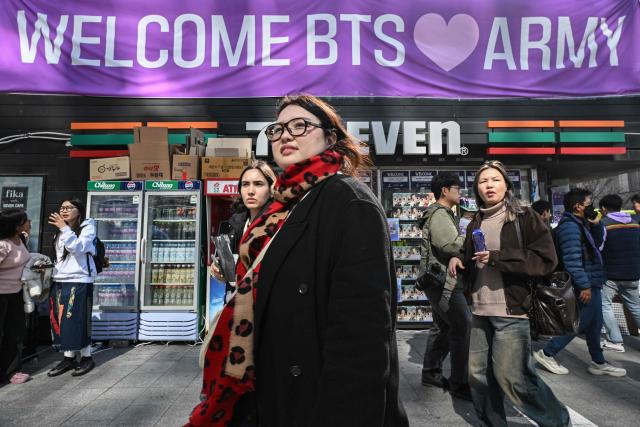 People walk past a convenience store with a banner welcoming BTS fans near the venue of the comeback concert of K-pop boy group BTS in downtown Seoul on March 21, 2026. South Korean megastars BTS reunite on March 21, for their first show in nearly four years, with an expected 260,000 fans taking over central Seoul for a K-pop extravaganza livestreamed to millions more worldwide. (Photo by Jung Yeon-je / AFP)